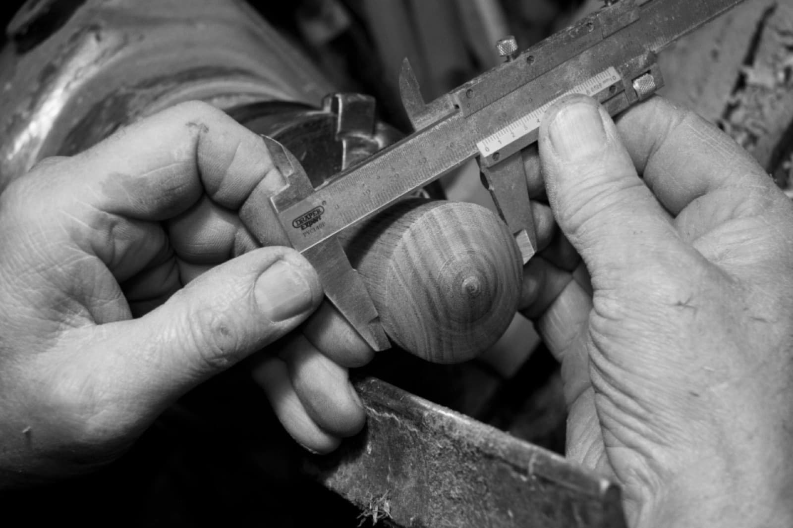 Les mains d'un artisan mesurant une pièce de bois tournée au pied à coulisse